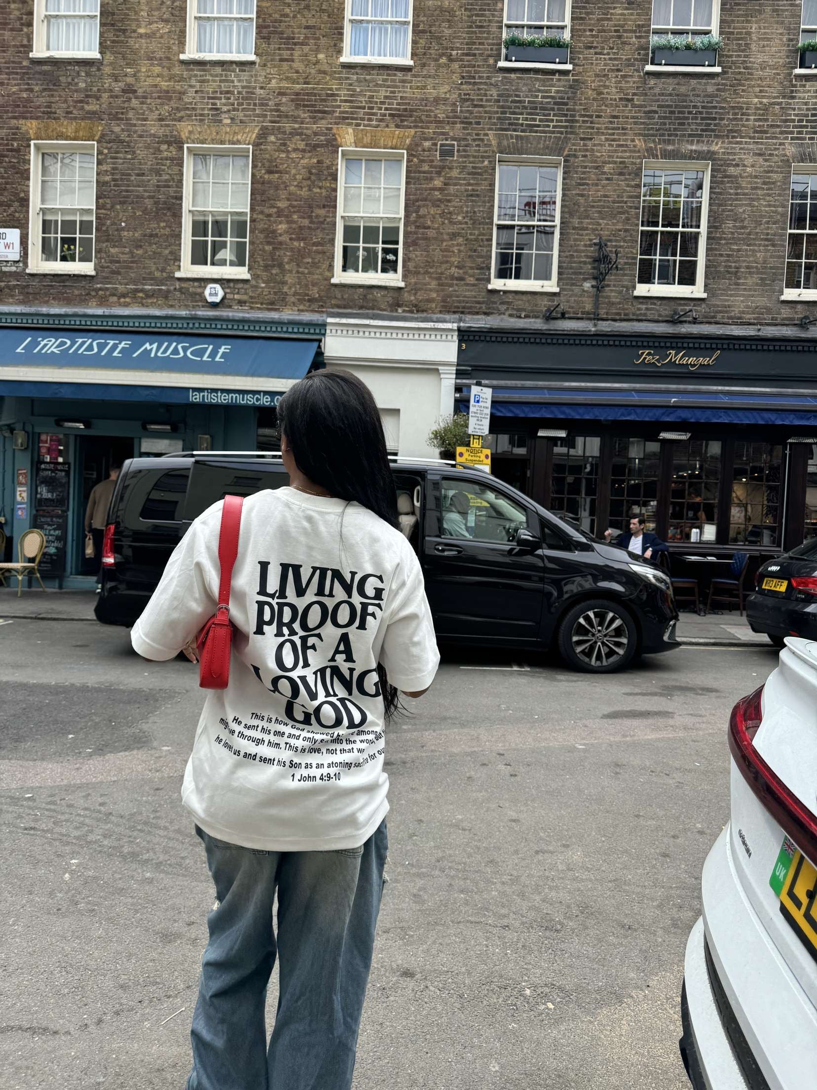 Person wearing a white Living Proof of a living God t-shirt with text walking on a street in an urban setting. #PhocusbyTimmy
